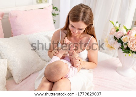 a young beautiful mother holds her daughter a girl of 6 months on her lap on a white bed, playing and kissing her, place for text