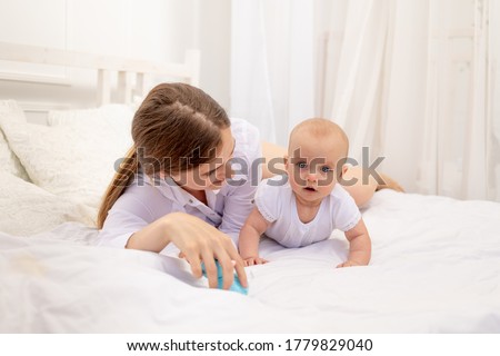 mom playing with baby 6 months lying on a white bed, leisure mom with baby, place for text
