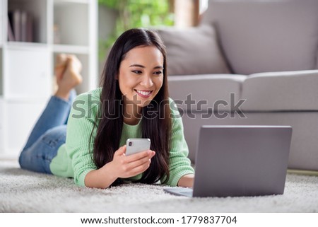 Close up photo of positive korean girl use laptop smartphone have free time search social media post repost lie floor carpet in house indoors