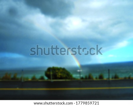 The blurred beautiful and colorful rainbow on the sea or ocean with cloudy sky from rain near coastline with empty road.