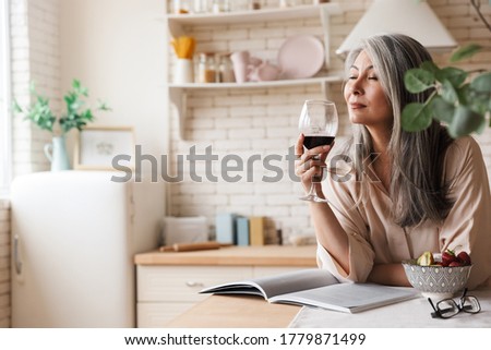 Picture of mature amazing pretty woman sitting at the kitchen indoors at home drinking wine