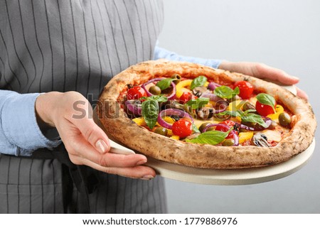 Woman holding tasty vegetable pizza on light grey background, closeup
