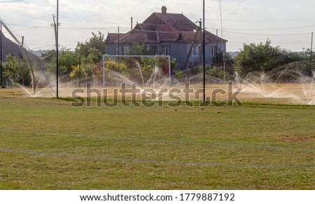 Fountains spraying water for irrigation of green grass of sports football field of stadium. Watering green grass field of stadium
