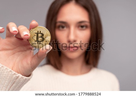 Blurred female demonstrating bitcoin coin to camera while advertising cryptocurrency against gray background