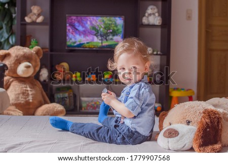 Cute baby boy and his dog plush toy watching TV sitting on a couch in the living room at home