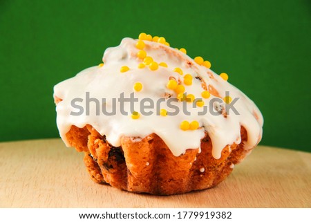 Cupcake, glazed rosy cupcake sprinkled with yellow sweet topping. On a wooden board with a green background.