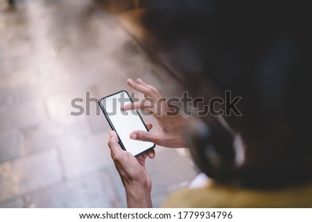 Cropped image of man holding smartphone with blank monitor using navigation application for searching locations, top view of male holding mobile phone checking news and videos from social networks