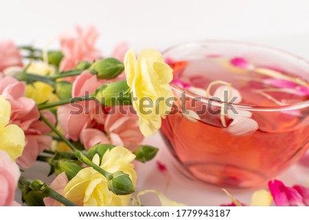Macro photo of yellow and pink flowers with glass tea cup. Fresh rose drink with spring flowers bouquet closeup