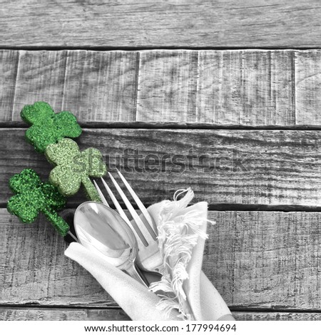 Green Shamrocks with black and white fork and spoon and napkin on rustic wood board background for St. Patricks Day Celebration.  Room or space for copy, text, words.