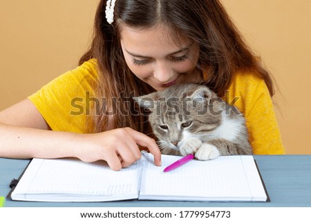 Girl learning with notebook at home on the table with her kitten. 
