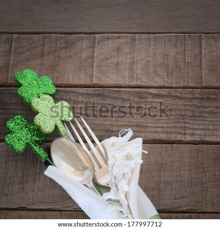 St. Patrick's Day green Shamrocks with fork, spoon, and napkin on rustic brown wood board background with room or space for copy, text, words.  Square