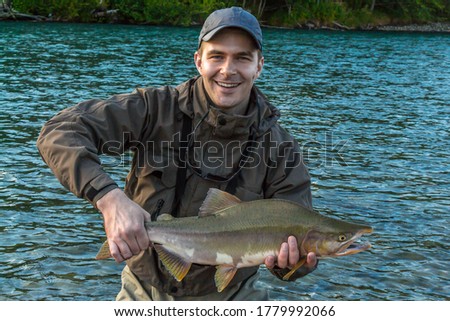 A fisherman holding up a large pink `humpback` salmon at sunset on a river in British Columbia, Canada Royalty-Free Stock Photo #1779992066