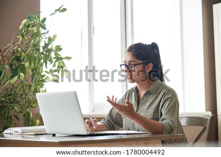 Indian woman online tutor remote teacher wearing glasses speaking to webcam chat explaining online class zoom video call school lesson looking at laptop virtual conference meeting work at home office. Royalty-Free Stock Photo #1780004492