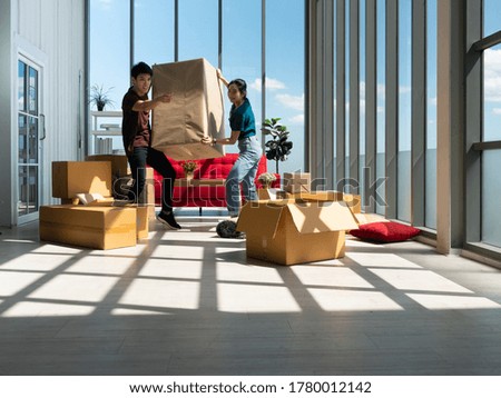 Asian young couple man and woman holding and carrying big cardboard while point out finger the way to moving box position after relocation from apartment to new home within many parcel or carton Royalty-Free Stock Photo #1780012142