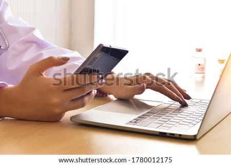 female doctor's hand is holding smartphone and  fingers to keyboard on notebook computer to working, business communications working with selective focus on

