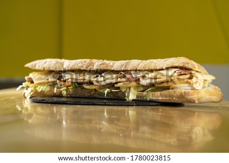 A closeup shot of a delicious sandwich with a baguette on a black round board on a wooden table