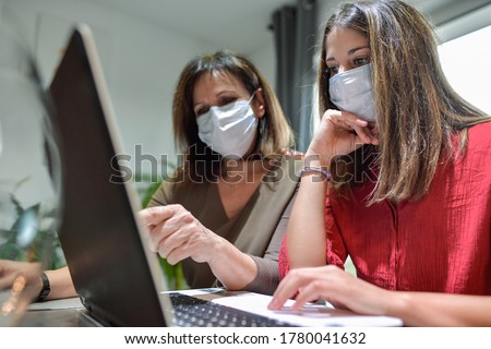 Student and her teacher wearing protective mask and working a lesson on  a laptop at home during lockdown due to covid-19 Royalty-Free Stock Photo #1780041632