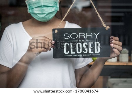 woman holding sign "sorry we are closed please come back again" on cafe or restaurant.