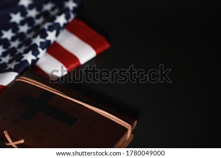 American flag and holy bible book on mirror background. Symbol of the United States and religion. Bible and striped flag on a black background.