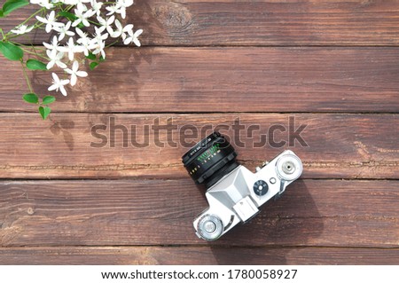an old retro film camera with a black lens is pointed towards white flowers on a wooden table made of boards with a copy space in the lower right corner of the image, a photo shoot.