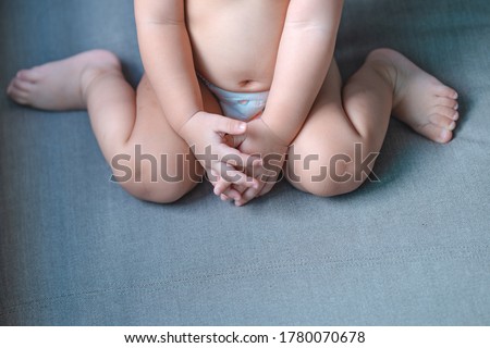 Little baby sitting W posture on the gray sofa,Which is called W-sitting knees bent and feet positioned outside hips can cause to hip dislocation. Royalty-Free Stock Photo #1780070678