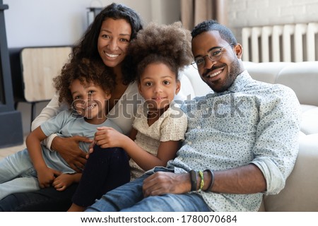 Portrait of smiling young african American family with two small kids sit relax on couch in living room together, happy biracial mom and dad hug cuddle with little children at home, show love care