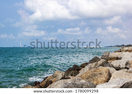 A view of the green sea, blue sky, cloudy sky, and rocks at the right corner of the picture.