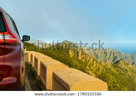Beautiful panorama of green mountains in Anaga rural park, covered with low clouds. And a part of car parked on mirador. Blue sky above. Tenerife, Canary Islands, Spain