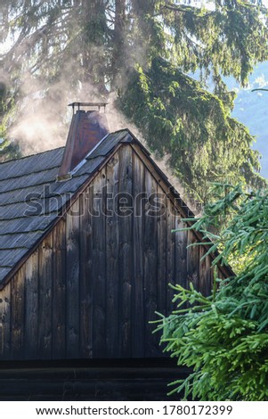 In the morning after a storm, water evaporates from the roof of an old wooden hut. Wooden cottage lit by the sun's rays