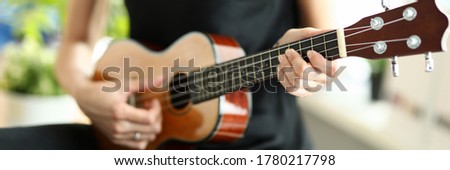 Close-up of person playing melody on ukulele. Female elegant hand pressing on string. Musical talent. Simple black dress on artist. Musical instrument and hobby concept