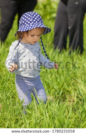 Adorable little girl with blue hat walking on the grass, note shallow depth of field.