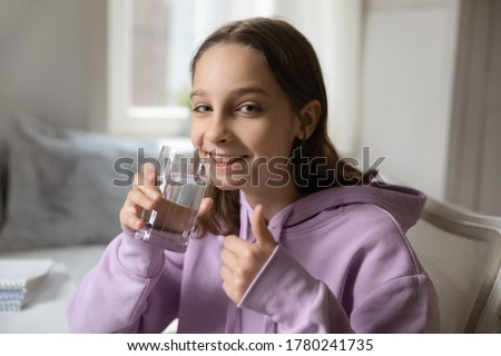 Head shot portrait smiling teenage girl holding glass of pure mineral water, teenager showing thumb up, recommending drinking water every day, healthy lifestyle and refreshment concept