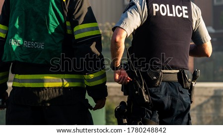 A firefighter and police officer standing one next to each other at a crime scene.  Royalty-Free Stock Photo #1780248842