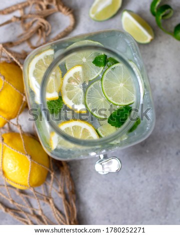 Lemonade in a glass jug with a non-standard view from above. Lemons in a string bag. Zero waste. Refreshing summer lemonade with lime lemon and mint. Spiral and lime wedges
