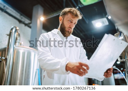 Caucasian male professional  technologist expert in white suit  operating production machine in food factory and doing quality control and holding checklist. Checking production in food industry.


