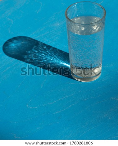 a glass of water, illuminated by the bright rays of the sun, with a beautiful shadow on a blue background