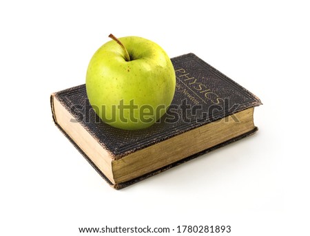 Picture. Green apple lies on the physics book of Isaac Newton on a white background