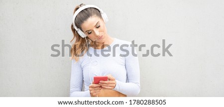 Nice smiling woman listening music with smartphone and headphones on city street. Relaxing time after jogging. Healthy lifestyle.