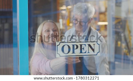 Two cheerful aged small business owners smiling while putting open sign at cafe entrance door. Senior couple entrepreneurs opening new restaurant. Small business and retirement concept