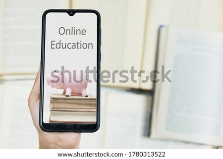 Cost of online education. Person hold smartphone with image of piggy bank and books. Copy space