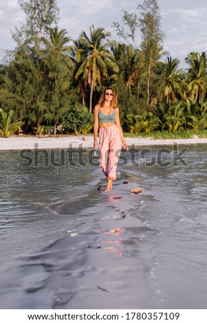 Happy beautiful young european woman with plastic bottle of water in her hand. Clean mineral water are good for health and recovery concept. Outdoor portrait, tropical beach sunset. Woman in crop top