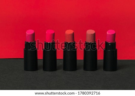 Five bottles of lipstick on a red and black background. Cosmetics for lips.