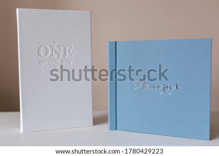 Comparison of photobook and photo box. Blue wedding book and white photo box on white wooden table