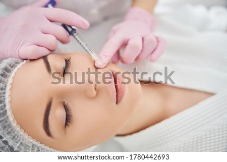 Charming woman undergoing upper lip injection while resting with closed eyes