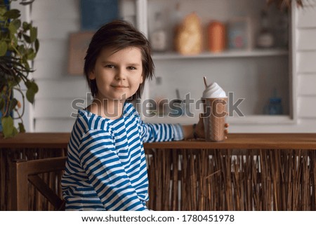 Young boy 10-12 years old in the striped shirt sits in a cafe and drinks a milkshake. Studio shot. Concept of vacation and holidays