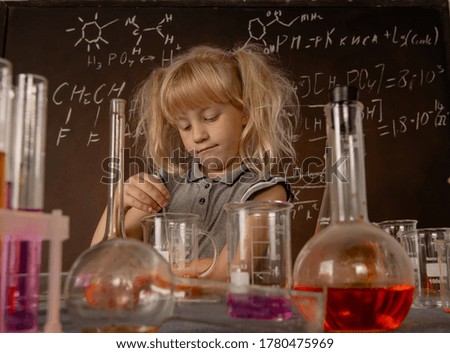 Curious little blonde girl with test tubes stirring orange colourful liquid in laboratory glass. Small kid observes chemical reaction. Biology education concept.