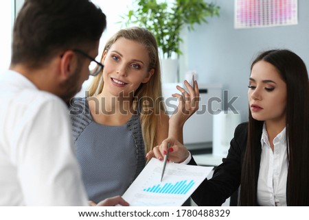 Bearded male manager is discussing economic chart with two cheerful female colleagues with pens at work