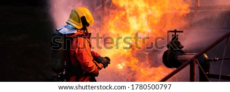 Panoramic Firefighter use water fog type fire extinguisher to fight with fire flame from oil pipeline leak and explosion on oil rig and natural gas station. Firefighter and industrial safety concept. Royalty-Free Stock Photo #1780500797