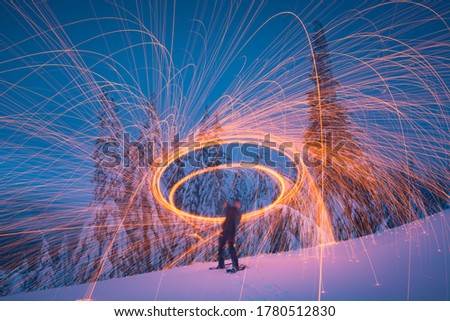 Man in a winter snowy forest painting by light with steel wool. Breathtaking picture.