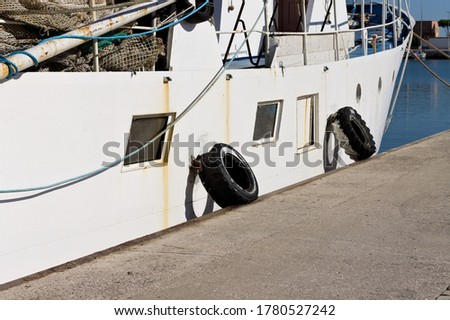 Old white fishing boat with fishing equipment and tires as fender (Pesaro, Italy, Europe)